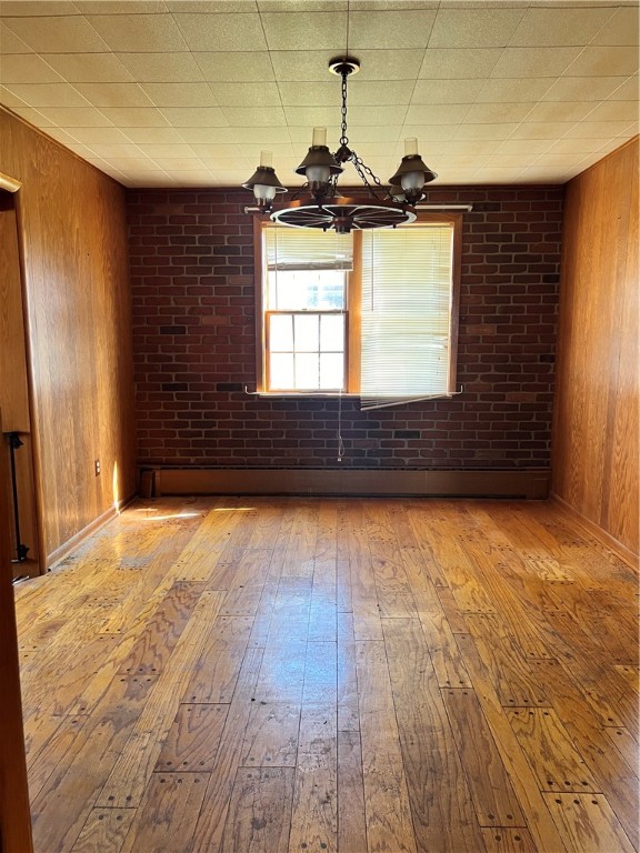 unfurnished room featuring an inviting chandelier, wood walls, and light hardwood / wood-style floors