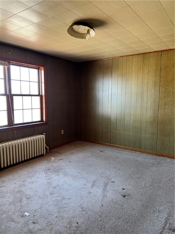 unfurnished room featuring wood walls, radiator, and carpet