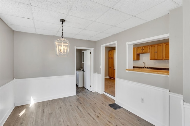 unfurnished room featuring sink, a chandelier, a drop ceiling, and light wood-type flooring