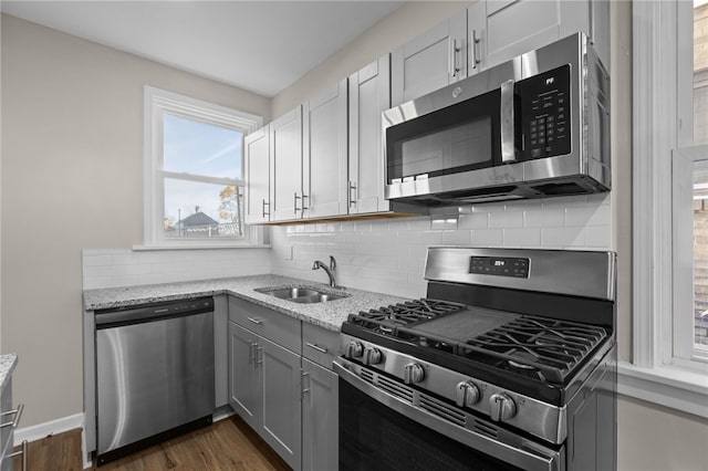 kitchen with stainless steel appliances, tasteful backsplash, dark wood-type flooring, sink, and light stone counters