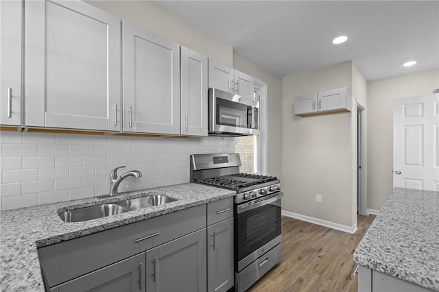 kitchen featuring light stone countertops, appliances with stainless steel finishes, backsplash, light wood-type flooring, and sink