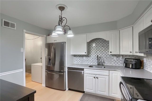 kitchen with sink, appliances with stainless steel finishes, decorative light fixtures, white cabinetry, and light wood-type flooring