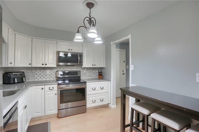 kitchen with white cabinets, backsplash, hanging light fixtures, and appliances with stainless steel finishes