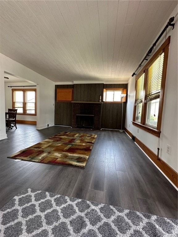 unfurnished living room with plenty of natural light, a brick fireplace, and dark wood-type flooring