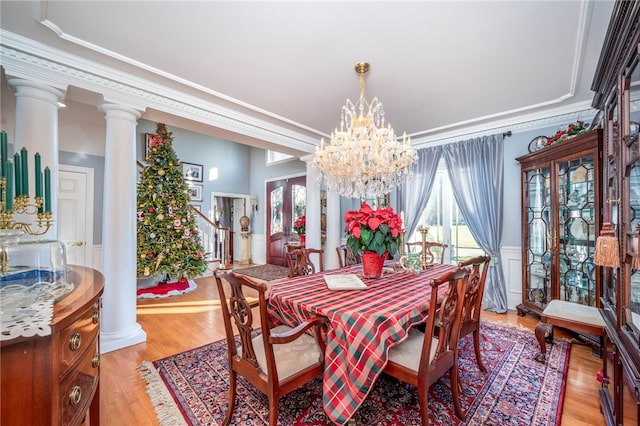 dining room with ornamental molding, a notable chandelier, decorative columns, and light wood-type flooring