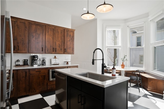 kitchen featuring stainless steel appliances, a center island with sink, light tile flooring, sink, and pendant lighting