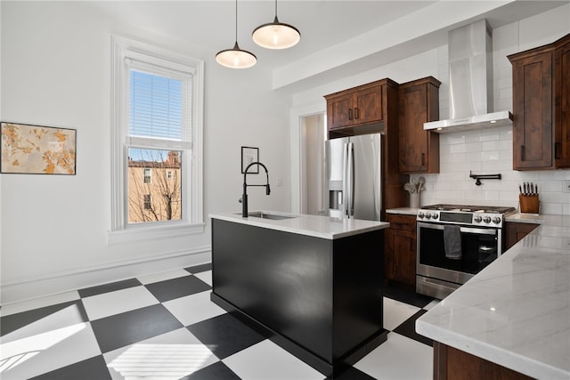 kitchen with a kitchen island with sink, hanging light fixtures, wall chimney range hood, stainless steel appliances, and tasteful backsplash