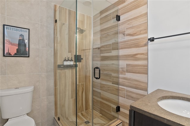 bathroom with a shower with door, tile walls, vanity, and toilet