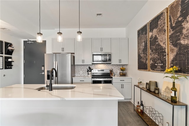 kitchen featuring a kitchen island with sink, pendant lighting, light stone counters, appliances with stainless steel finishes, and dark wood-type flooring