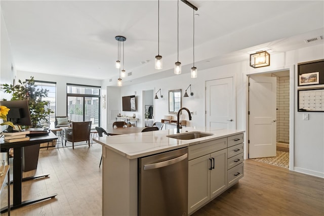 kitchen with pendant lighting, stainless steel dishwasher, light hardwood / wood-style floors, sink, and light stone counters