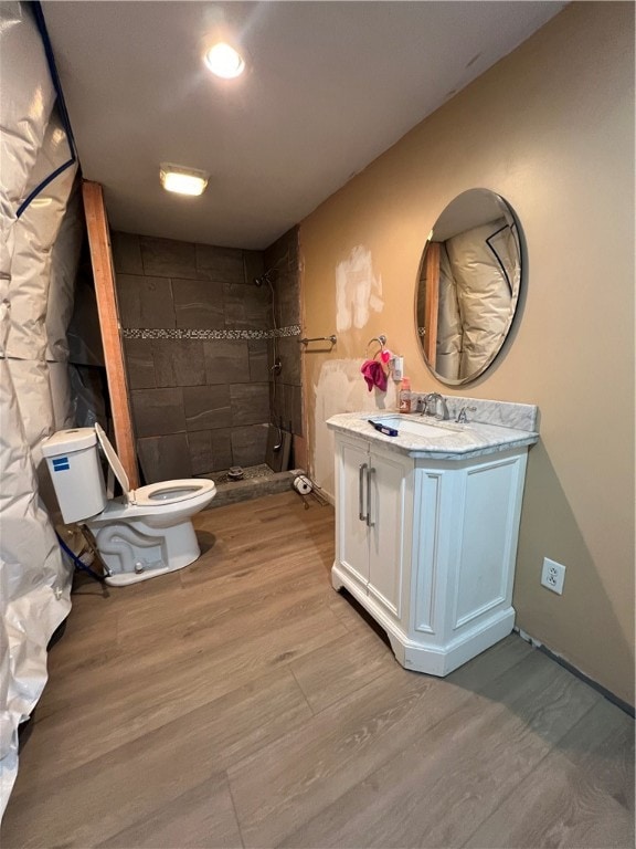 bathroom featuring toilet, wood-type flooring, tiled shower, and vanity with extensive cabinet space