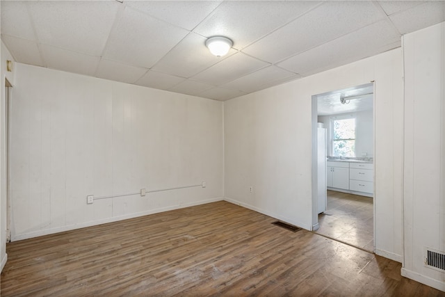 empty room with a paneled ceiling, wood walls, and hardwood / wood-style floors