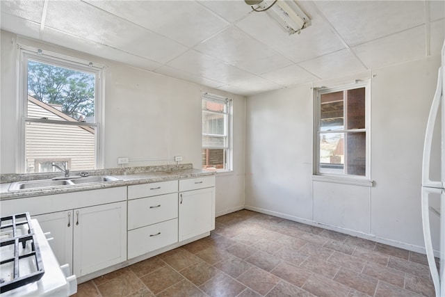 kitchen with white fridge, white cabinetry, sink, and cooktop