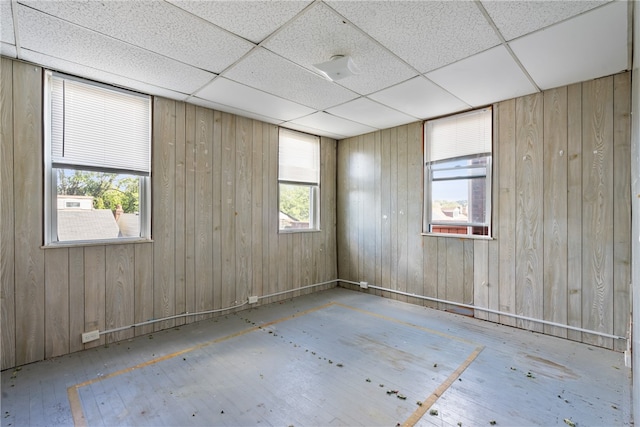 unfurnished room featuring wooden walls, a drop ceiling, and a healthy amount of sunlight