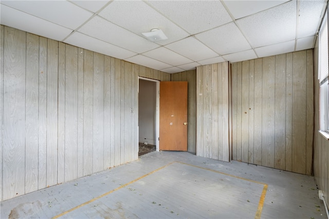 unfurnished room featuring a drop ceiling and wood walls