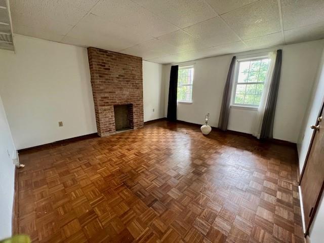 unfurnished living room featuring a paneled ceiling, a fireplace, and parquet flooring