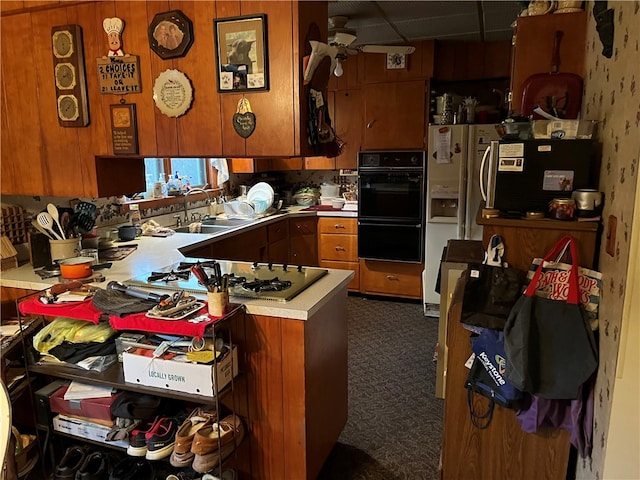 kitchen with black double oven, dark colored carpet, ceiling fan, sink, and kitchen peninsula