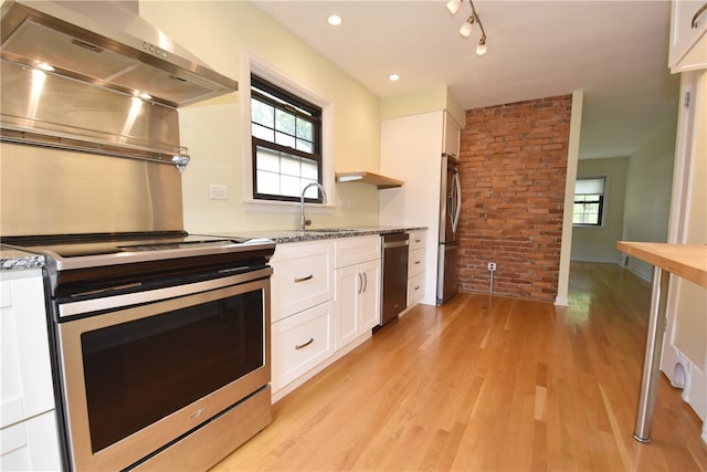 kitchen featuring light stone counters, stainless steel appliances, wall chimney range hood, sink, and white cabinets