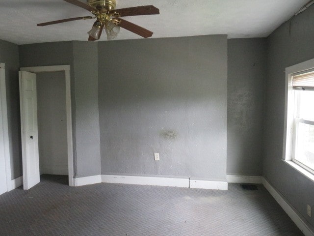 spare room featuring a wealth of natural light, dark carpet, and ceiling fan