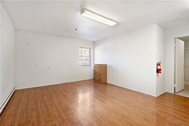 spare room with baseboard heating, light hardwood / wood-style floors, and a textured ceiling