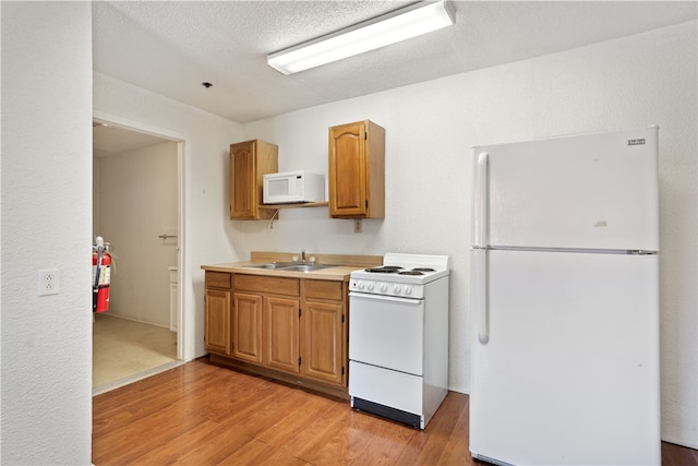 kitchen with white appliances, light hardwood / wood-style flooring, sink, and a textured ceiling