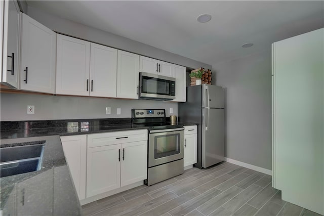 kitchen featuring appliances with stainless steel finishes, sink, white cabinets, and dark stone countertops