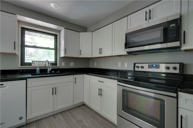 kitchen with stainless steel appliances, white cabinetry, dark stone countertops, sink, and light wood-type flooring