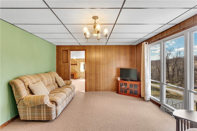 carpeted living room with wooden walls, a drop ceiling, and a chandelier