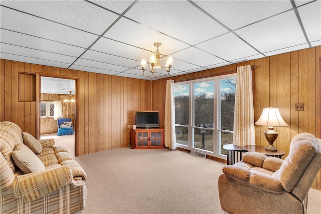 living room with an inviting chandelier, a drop ceiling, light carpet, and wood walls