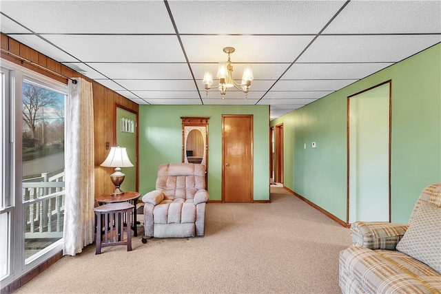 living area featuring light colored carpet, wood walls, a chandelier, and a paneled ceiling