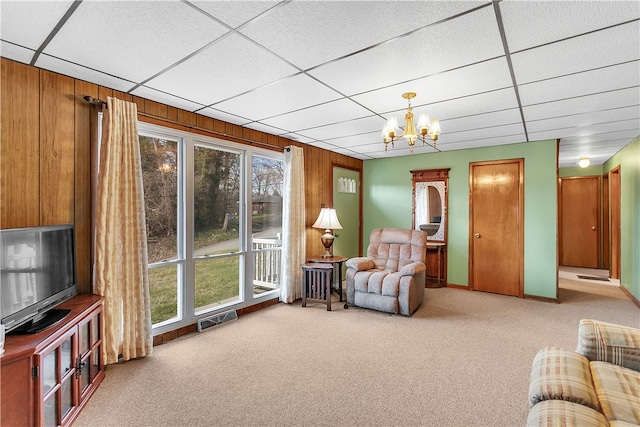 living room featuring a chandelier, wood walls, light carpet, and a drop ceiling