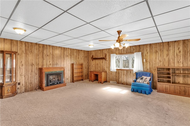 unfurnished room with carpet, a paneled ceiling, wood walls, and ceiling fan