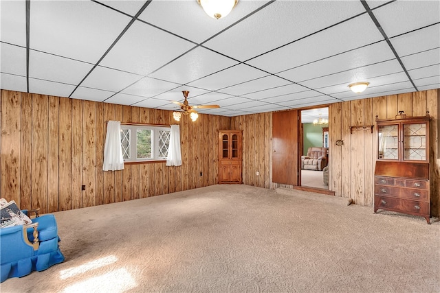 unfurnished room featuring carpet floors, wood walls, ceiling fan, and a drop ceiling