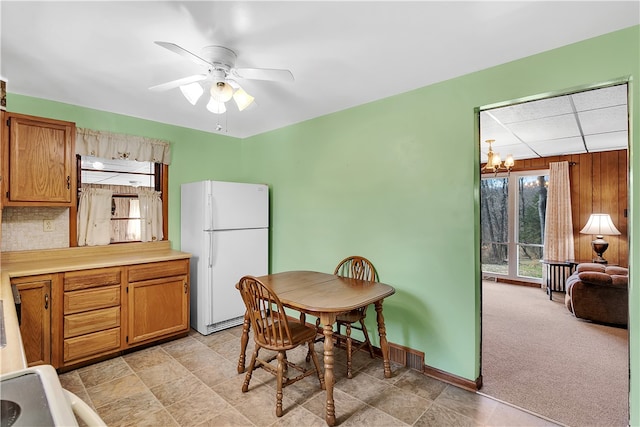 dining area with light carpet, wood walls, and ceiling fan with notable chandelier