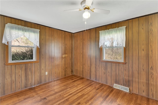 unfurnished room featuring wood walls, hardwood / wood-style floors, a healthy amount of sunlight, and ceiling fan