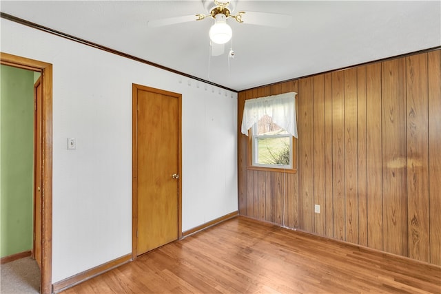 spare room featuring wood walls, ceiling fan, and light wood-type flooring