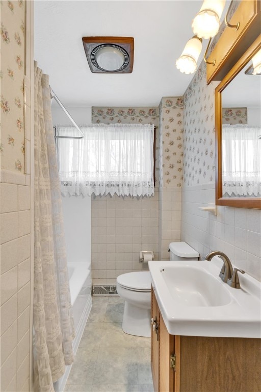 full bathroom featuring a wealth of natural light, large vanity, toilet, and tile walls