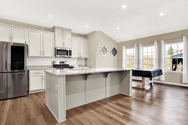 kitchen with lofted ceiling, wood-type flooring, appliances with stainless steel finishes, and a kitchen island with sink