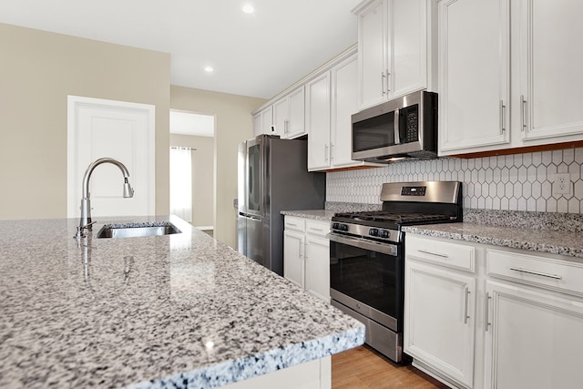 kitchen featuring tasteful backsplash, stainless steel appliances, light stone counters, sink, and white cabinets