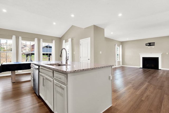 kitchen featuring a kitchen island with sink, dark hardwood / wood-style flooring, light stone counters, sink, and vaulted ceiling