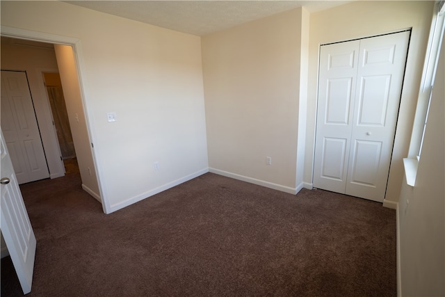 unfurnished bedroom with dark colored carpet and a closet