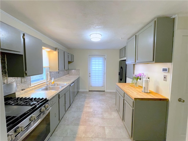 kitchen featuring light tile flooring, wooden counters, sink, stainless steel appliances, and tasteful backsplash