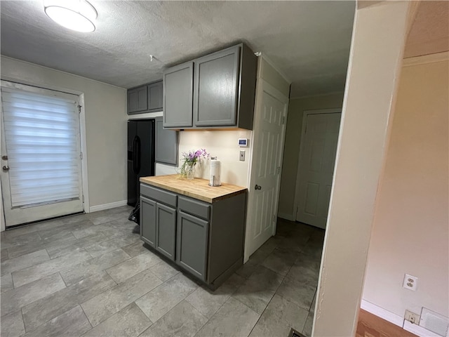 kitchen with light tile floors, a textured ceiling, wood counters, black fridge, and gray cabinets