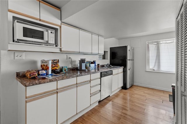 kitchen featuring appliances with stainless steel finishes, white cabinetry, sink, dark stone countertops, and light wood-type flooring