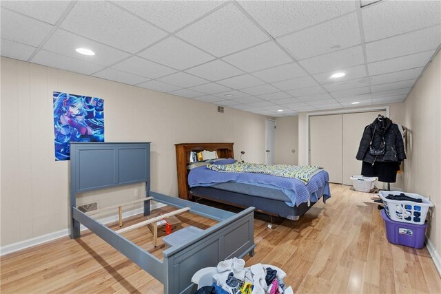 bedroom featuring a paneled ceiling, light wood-type flooring, and a closet