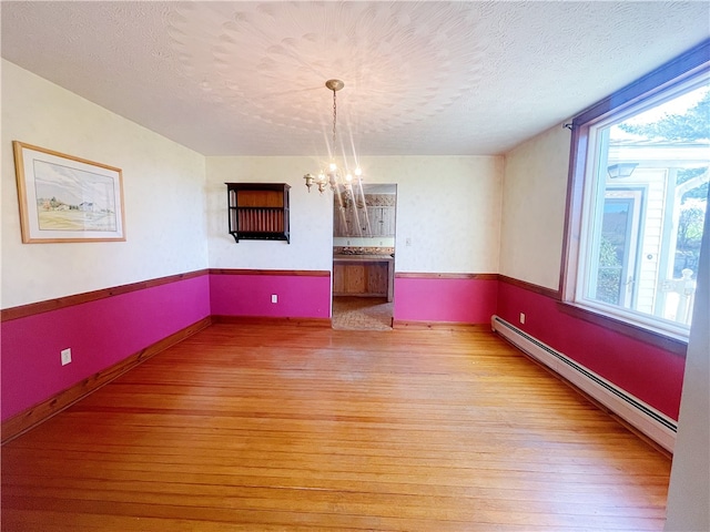 spare room featuring an inviting chandelier, light hardwood / wood-style flooring, a baseboard radiator, and a healthy amount of sunlight