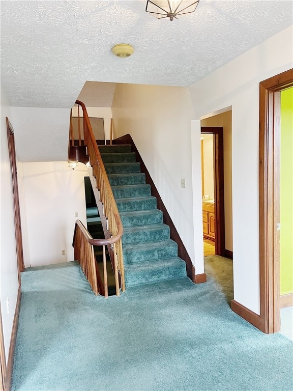 stairs with a textured ceiling and dark colored carpet