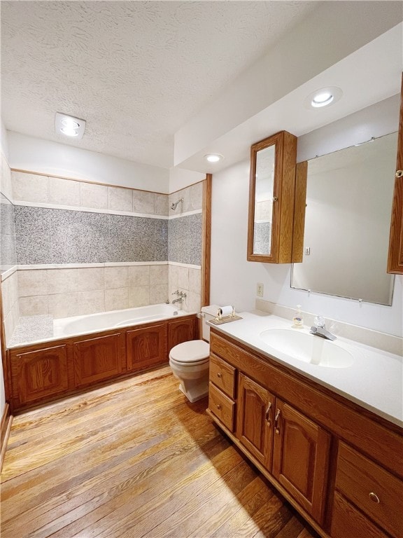 bathroom featuring a bathing tub, a textured ceiling, toilet, oversized vanity, and hardwood / wood-style flooring