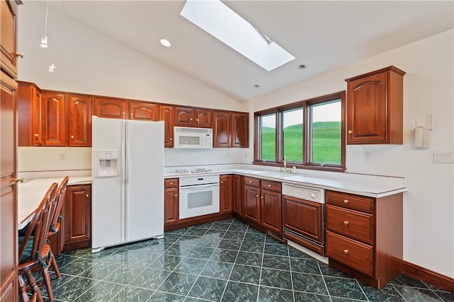 kitchen with a skylight, sink, white appliances, and dark tile patterned flooring