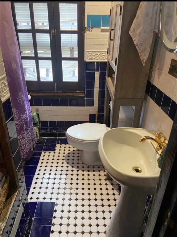 bathroom with tile flooring, tile walls, sink, and toilet